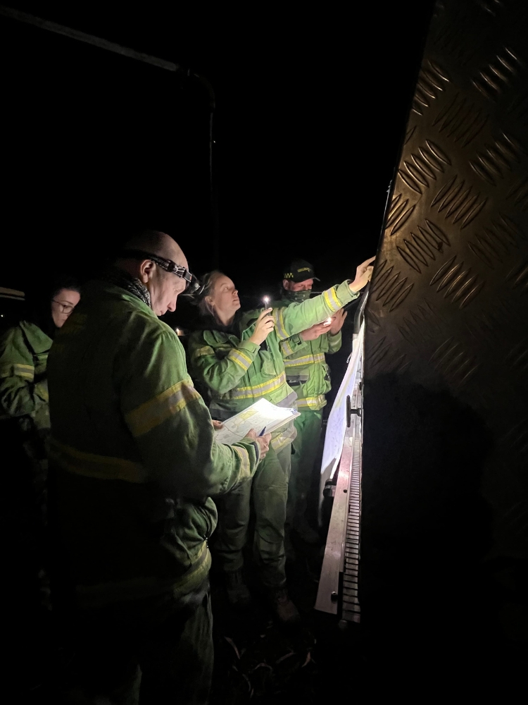 Staff in FFMVic uniforms in a dark room using torches to read papers