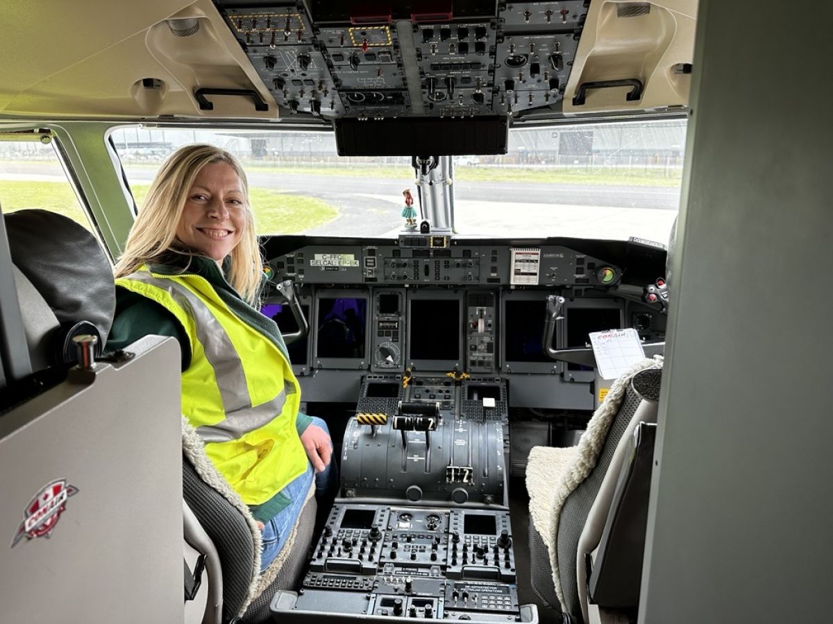 Sharon O'Sullivan wearing a fluoro yellow vest sitting in the cockpit of a Q400. She is turned around in her seat to look at the camera