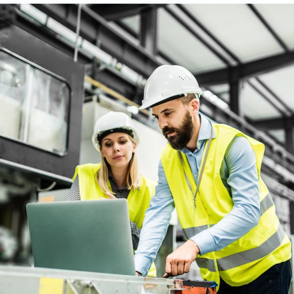 People in high visibilty vests and hard cats in a warerhouse looking at a computer